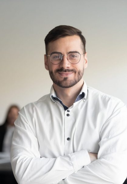 Confident happy young male manager in eyeglasses standing with folded hands head shot portrait. Smiling company owner, startup businessman, team leader, successful employee looking at camera.
